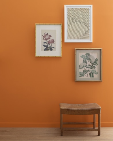 A Gold Rush-painted wall with three framed art pieces, a small bench, and a floor lamp.