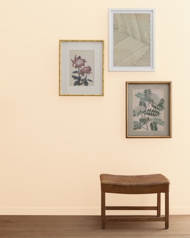A Pale Oats-painted wall with three framed art pieces, a small bench, and a floor lamp.
