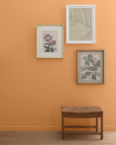 A Soft Pumpkin-painted wall with three framed art pieces, a small bench, and a floor lamp.