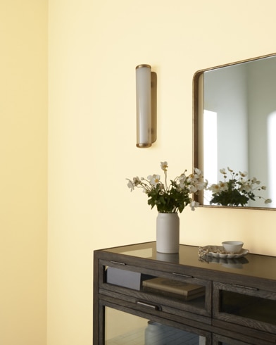 Una mesa marrón con un juego de té y un jarrón con flores debajo de un espejo colgado en una pared pintada de color Eres Mi Luz.
