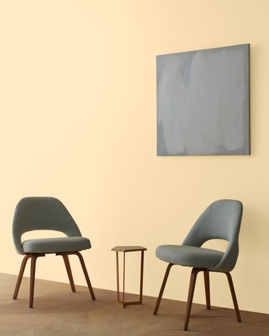 Two blue chairs and a table stand in front of a wall under an abstract painting hanging on a wall painted Birmingham Cream.