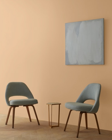 Two blue chairs and a table stand in front of a wall under an abstract painting hanging on a wall painted Farm Fresh.