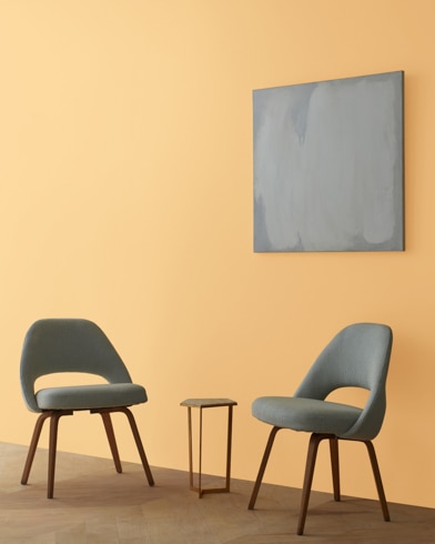 Two blue chairs and a table stand in front of a wall under an abstract painting hanging on a wall painted Orange Ice.