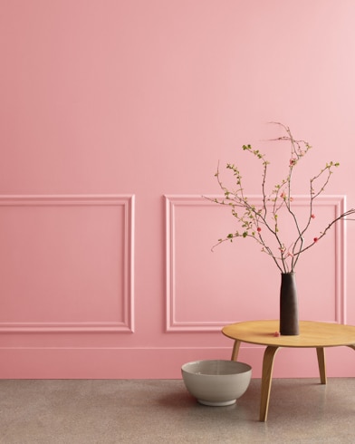 A midcentury wooden accent table and decor in front of a Delicate Rose-painted wall with rectangular molding.