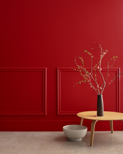 A midcentury wooden accent table and decor in front of a Heritage Red-painted wall with rectangular molding.
