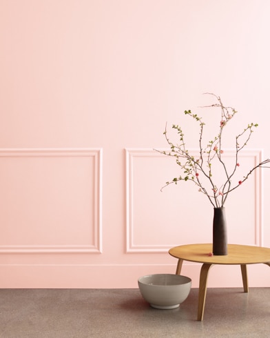 A midcentury wooden accent table and decor in front of a Touch of Pink-painted wall with rectangular molding.