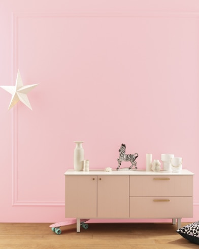 A modern white dresser with decor in front of a Authentic Pink-painted wall with square molding, and a dangling white star. 