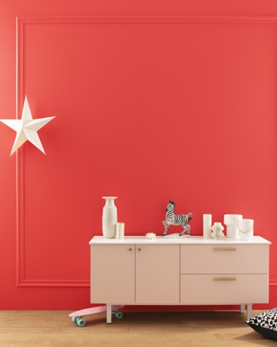 A modern white dresser with decor in front of a Bull's Eye Red-painted wall with square molding, and a dangling white star. 