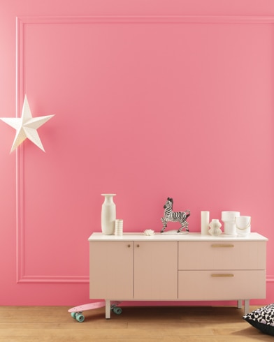 A modern white dresser with decor in front of a Flamingo's Dream-painted wall with square molding, and dangling white star. 