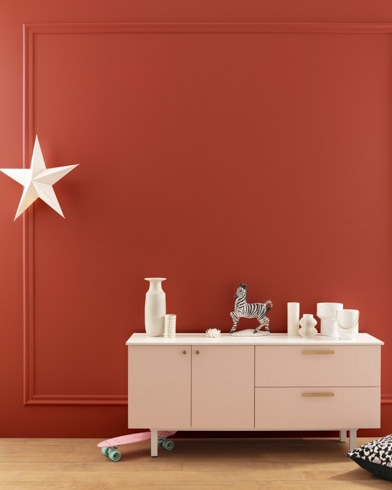 A modern white dresser with decor in front of a Merlot Red-painted wall with square molding, and a dangling white star. 