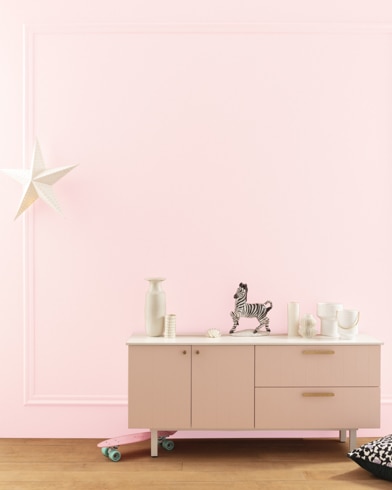 A modern white dresser with decor in front of a Pink Cadillac-painted wall with square molding, and a dangling white star. 
