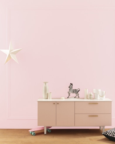 A modern white dresser with decor in front of a Pink Fairy-painted wall with square molding, and a dangling white star. 