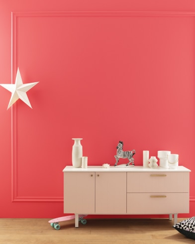 A modern white dresser with decor in front of a Rose Quartz-painted wall with square molding, and a dangling white star. 