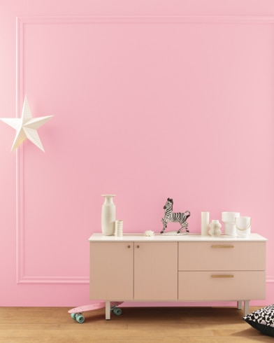 A modern white dresser with decor in front of a Tickled Pink-painted wall with square molding, and a dangling white star. 