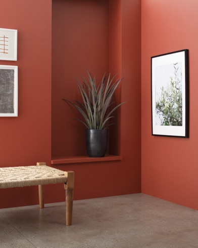 A wooden bench in front of a Iron Ore Red-painted wall with art and an inset shelf featuring a houseplant.