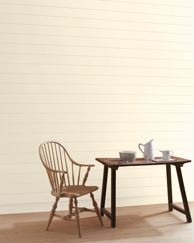 A Fine China-painted wall with wooden spindle chair and white pitcher, cup and bowl on a table.