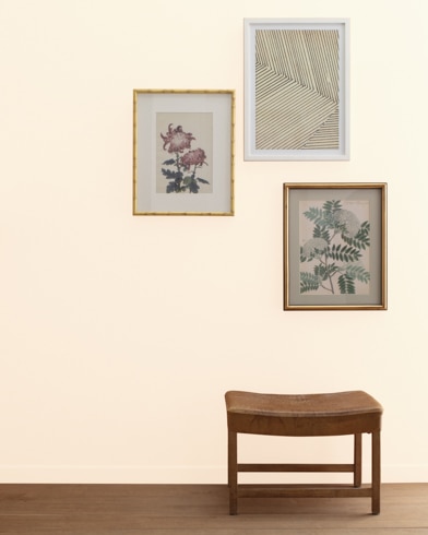 An Adobe White-painted wall with three framed art pieces, a small bench, and a floor lamp.