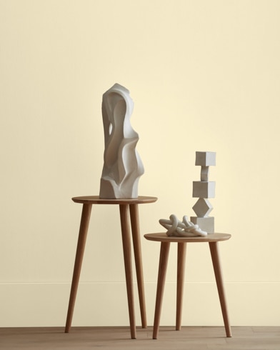 White abstract scupltures stand on wooden stools in front of a wall painted .