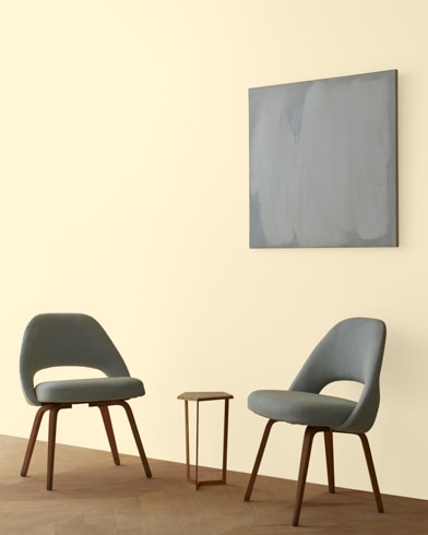 Two blue chairs and a table stand in front of a wall under an abstract painting hanging on a wall painted Corinthian White.