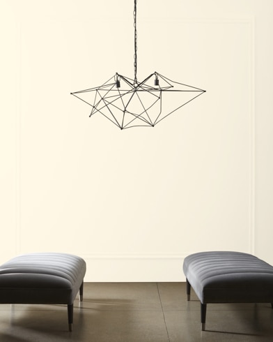 A modern, wiry chandelier hangs over two velvet ottomans in front of a wall painted White Cloud.