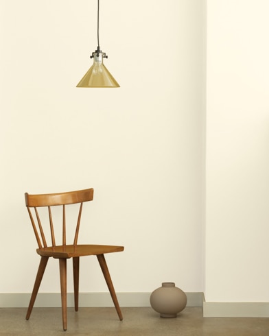 A single-bulb light hangs over a wooden chair and small ceramic pot in front of a wall painted Ivory Tusk.