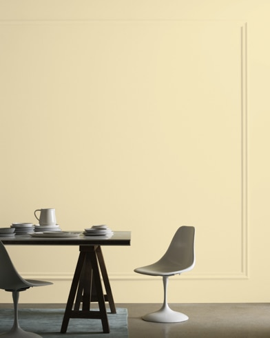 A midcentury modern dining table with two chairs sits in front of a wall painted Pale Moon.