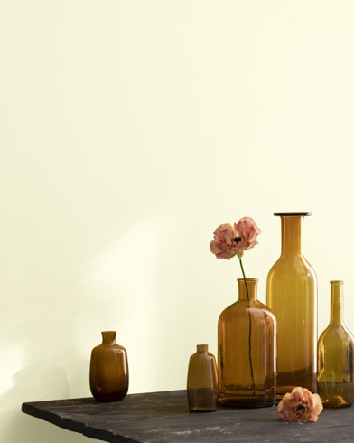 A collection of brown-tinted glass vases sit atop a wooden shop table next to a wall painted Lemon Ice.