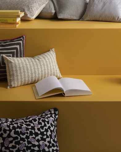 Graphic pillows and stacks of books on a multi-level reading nook painting in Luminous Days.
