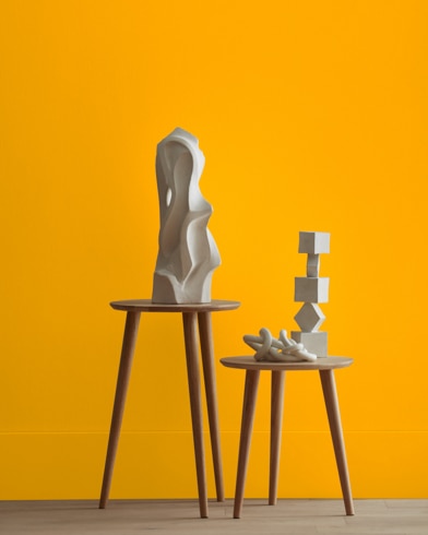 White abstract scupltures stand on wooden stools in front of a wall painted Bumble Bee Yellow.