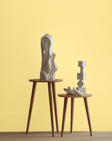 White abstract scupltures stand on wooden stools in front of a wall painted Mellow Yellow.