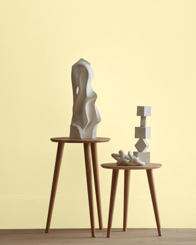White abstract scupltures stand on wooden stools in front of a wall painted Moonlight.