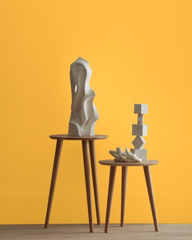 White abstract scupltures stand on wooden stools in front of a wall painted Oxford Gold.