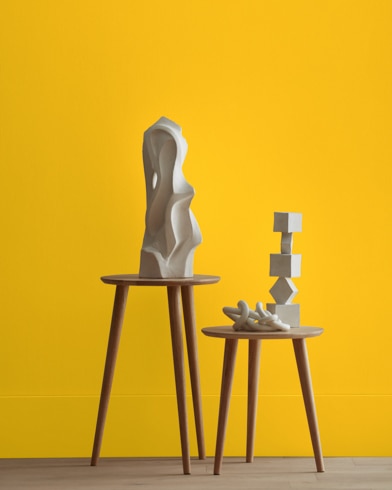 White abstract scupltures stand on wooden stools in front of a wall painted Sparkling Sun.