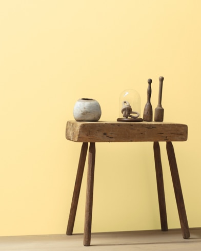Ceramic artifacts are placed on a modern wooden table in front of a wall painted Morning Sunshine.