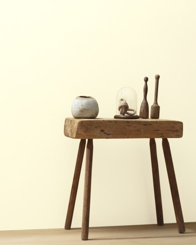 Ceramic artifacts are placed on a modern wooden table in front of a wall painted Pale Straw.