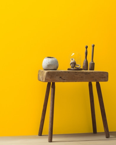 Ceramic artifacts are placed on a modern wooden table in front of a wall painted Yellow Flash.