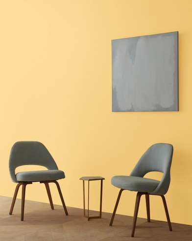 Two blue chairs and a table stand in front of a wall under an abstract painting hanging on a wall painted Beverly Hills.