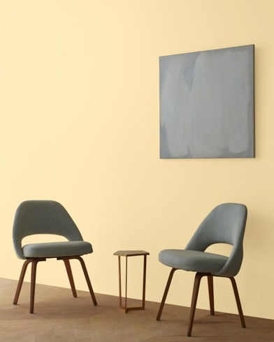 Two blue chairs and a table stand in front of a wall under an abstract painting hanging on a wall painted Golden Lab.