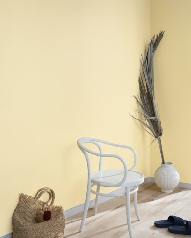 A palm frond, straw tote bag, black slide sandals and white metal chair lean against a wall painted America's Heartland.