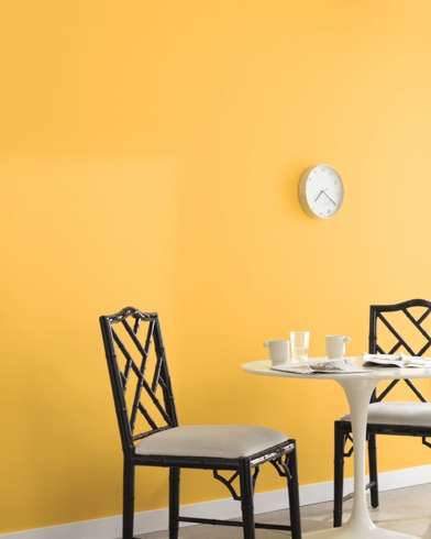 A clock hangs on a wall painted Happily Ever After in a room with a metal dining set and a potted plant on a wooden block.