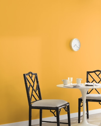 A clock hangs on a wall painted Sunflower Fields in a room with a metal dining set and a potted plant on a wooden block.