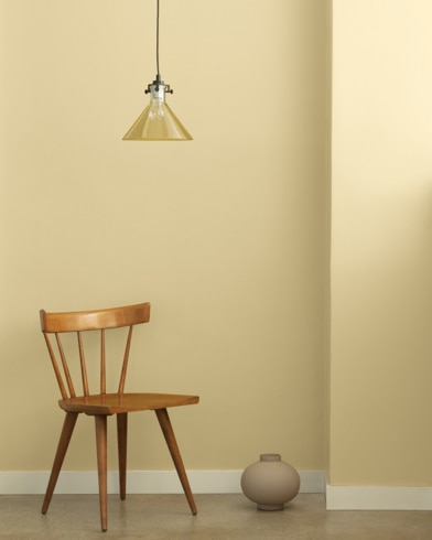 A single-bulb light hangs over a wooden chair and small ceramic pot in front of a wall painted Bronzed Beige.