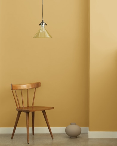 A single-bulb light hangs over a wooden chair and small ceramic pot in front of a wall painted Cork.