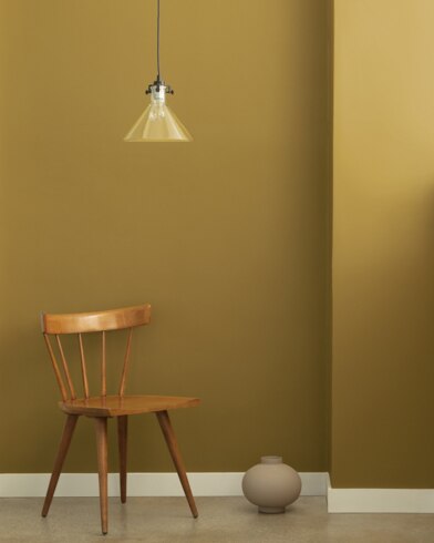 A single-bulb light hangs over a wooden chair and small ceramic pot in front of a wall painted Golden Chalice.