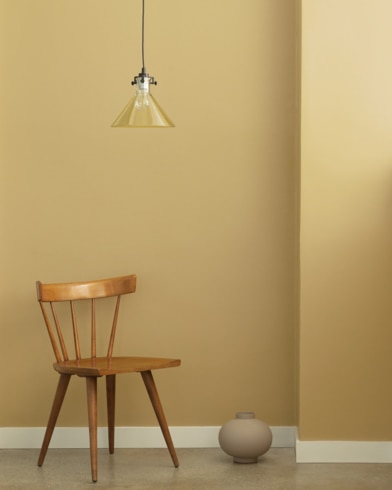 A single-bulb light hangs over a wooden chair and small ceramic pot in front of a wall painted Sulfur Yellow.