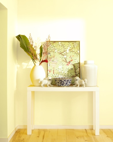 A white table with a collection of white vases, trinkets and abstract art sits against a Banan-Appeal-painted wall.
