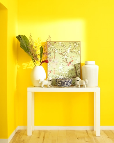 A white table with a collection of white vases, trinkets and abstract art sits against a Bright Yellow-painted wall.