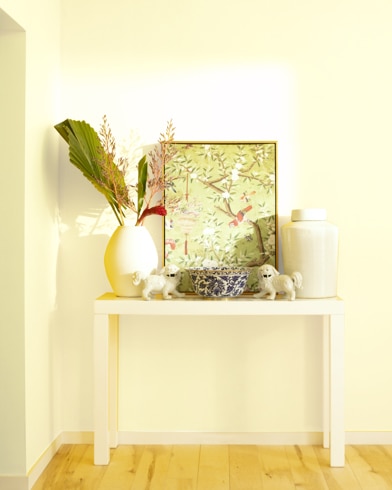 A white table with a collection of white vases, trinkets and abstract art sits against a Lemon Souffl�-painted wall.