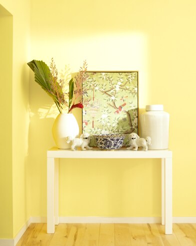 A white table with a collection of white vases, trinkets and abstract art sits against a Limon-painted wall.