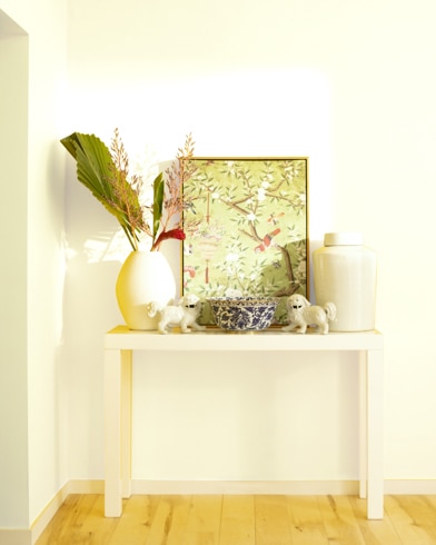 A white table with a collection of white vases, trinkets and abstract art sits against a Palm Coast Pale-painted wall.